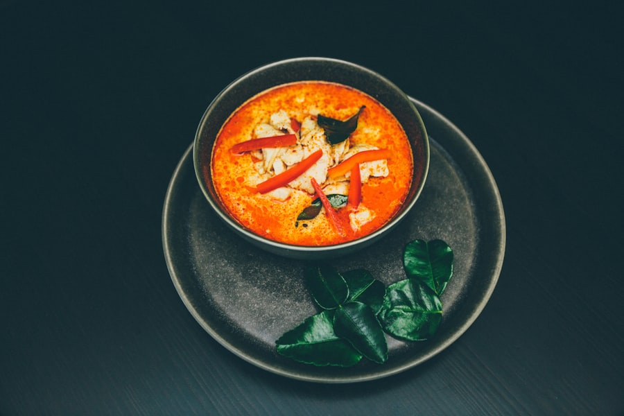 Bowl of spicy red soup garnished with chili and basil leaves on a dark plate