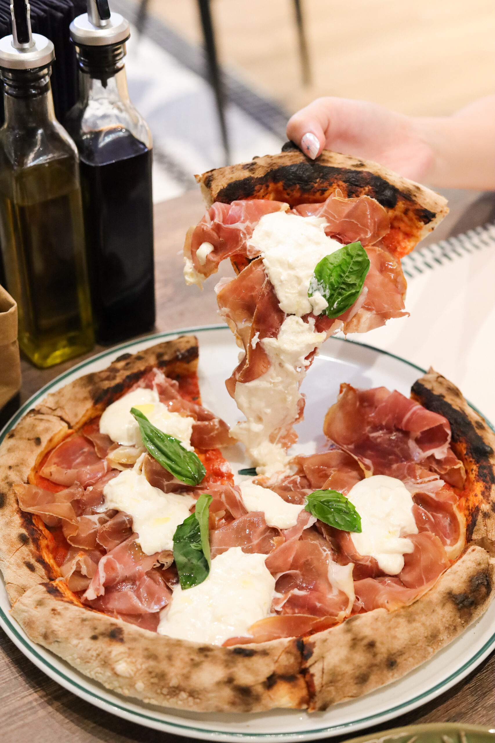 Lifting a slice of prosciutto and burrata wood-fired pizza at Bianca Bangkok