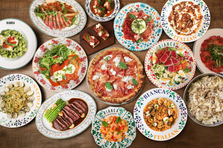 Overhead table of Bianca Italian dishes: wood-fired pizza, pasta, steak, salads and antipasti