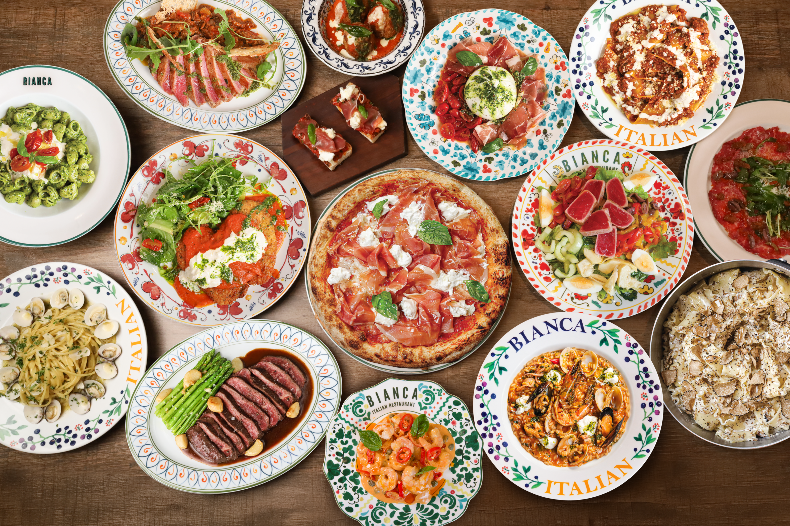 Overhead table of Bianca Italian dishes: wood-fired pizza, pasta, steak, salads and antipasti