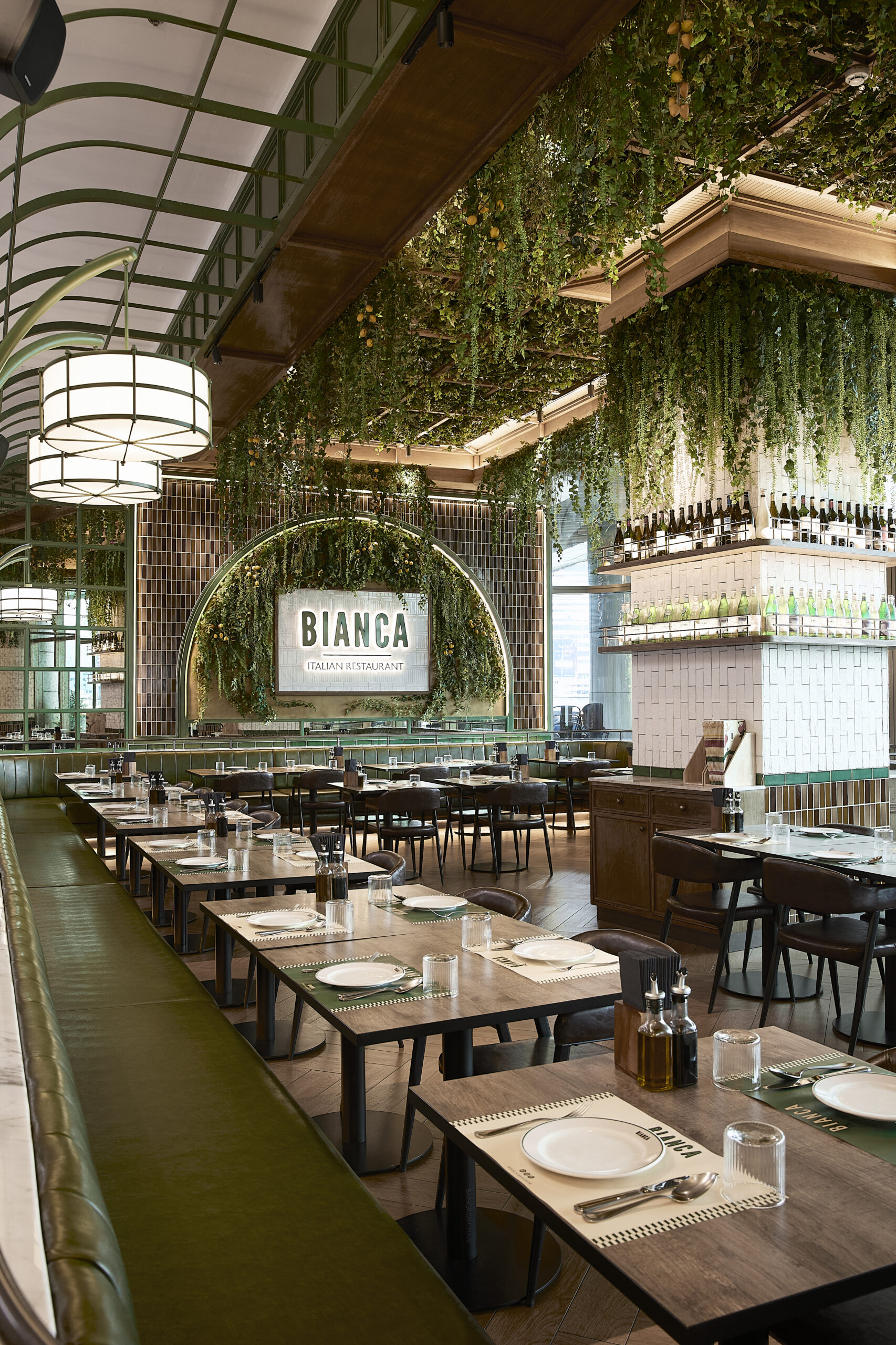 Long main dining hall at Bianca with green banquettes and hanging plants